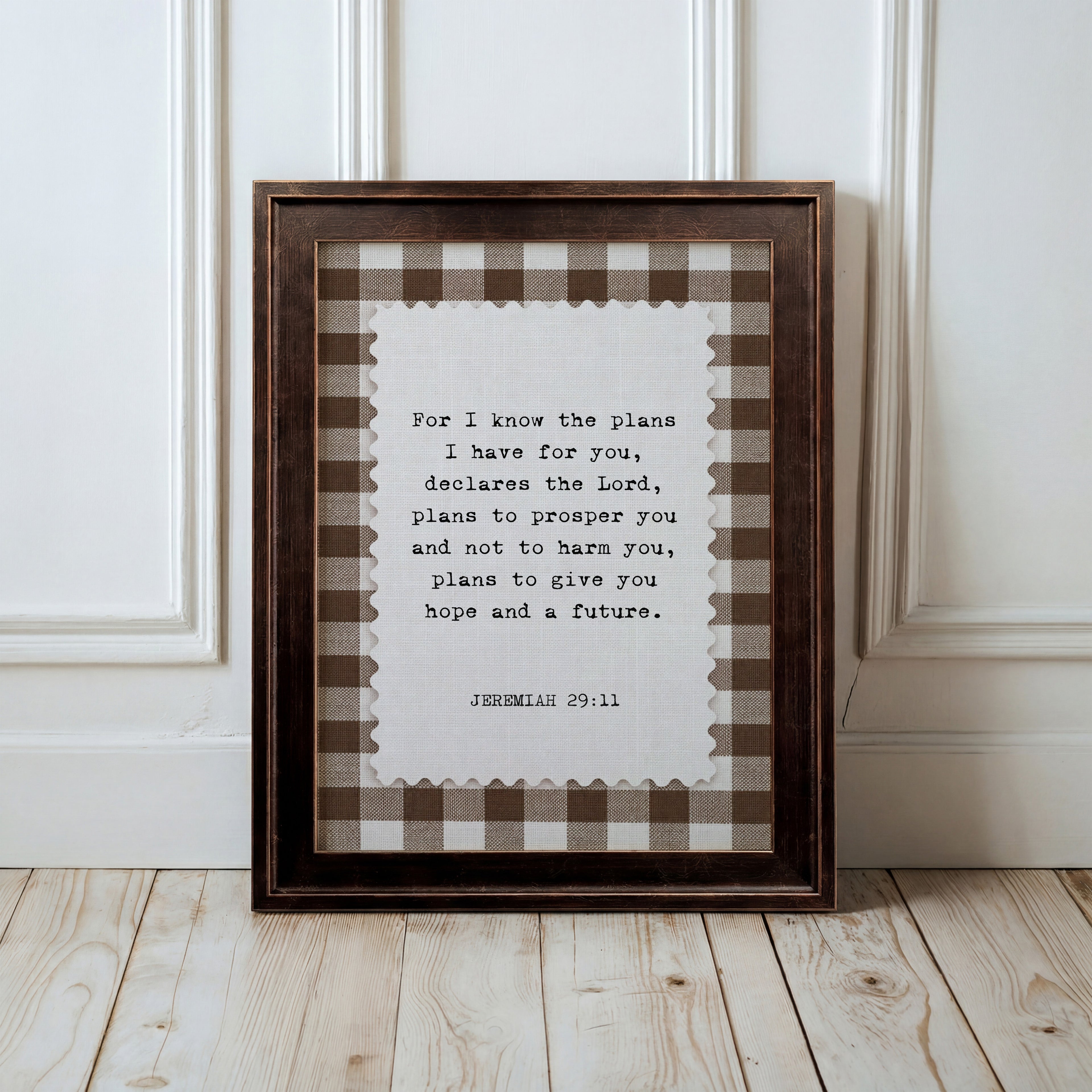 A framed print with a Bible verse from Jeremiah 29:11 is displayed on a wooden floor against a white wall.