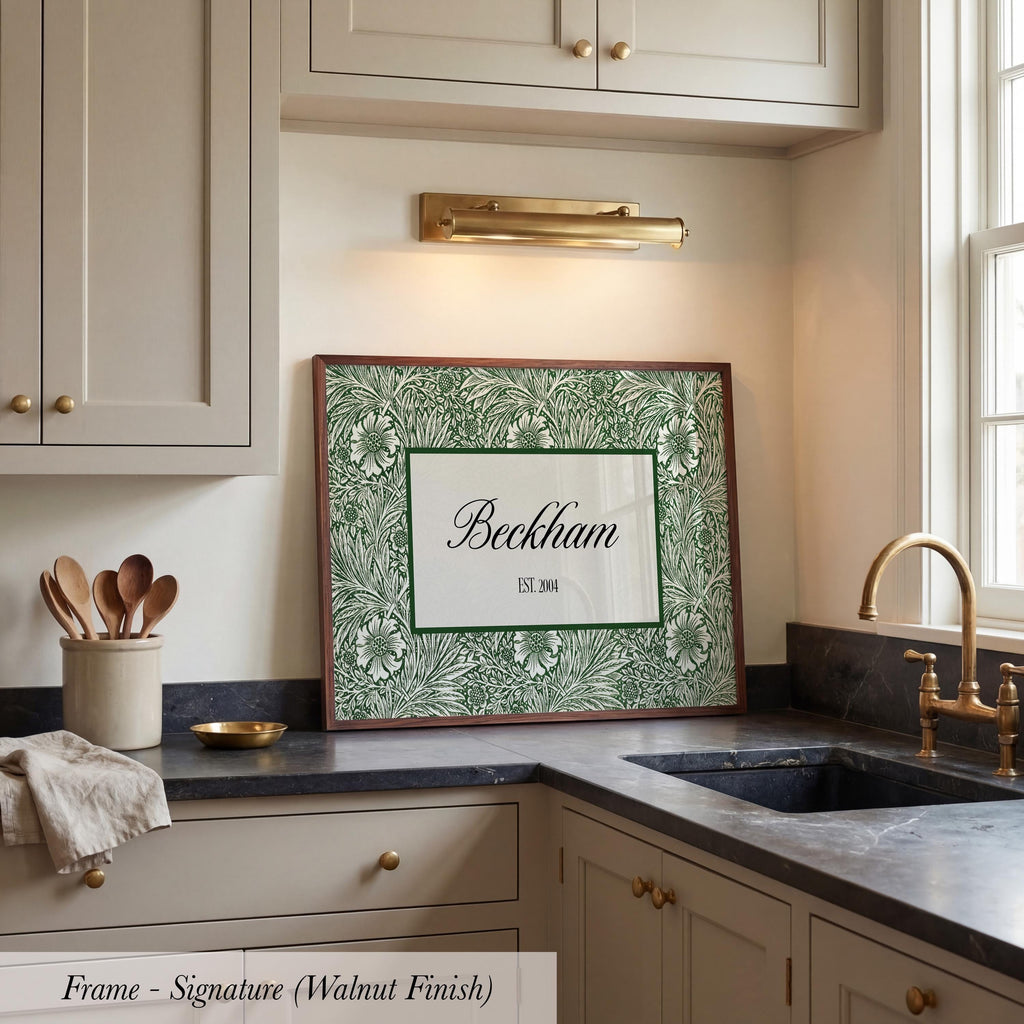 A framed artwork with a green floral pattern and the name "Beckham" is displayed on a kitchen counter, with a sink and cabinets in the background.