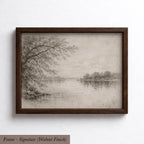 A framed black and white landscape painting depicting a serene lake surrounded by trees and a cloudy sky.
