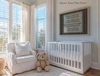 A cozy nursery with a white crib, a white armchair, and a teddy bear, all bathed in soft light from the large windows. A framed nursery rhyme is displayed on the wall above the crib, adding a touch of whimsy to the serene space.