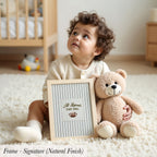 A young child sits on the floor, holding a framed sign that says "All Legends Start Small". Next to the child is a teddy bear.