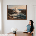 A woman is sitting at a table, reading a book, with a framed painting of a crashing ocean scene hanging on the wall behind her.