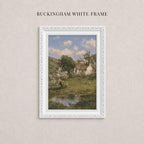 A white framed painting depicting a rural landscape with a pond, trees, and a small house in the background.