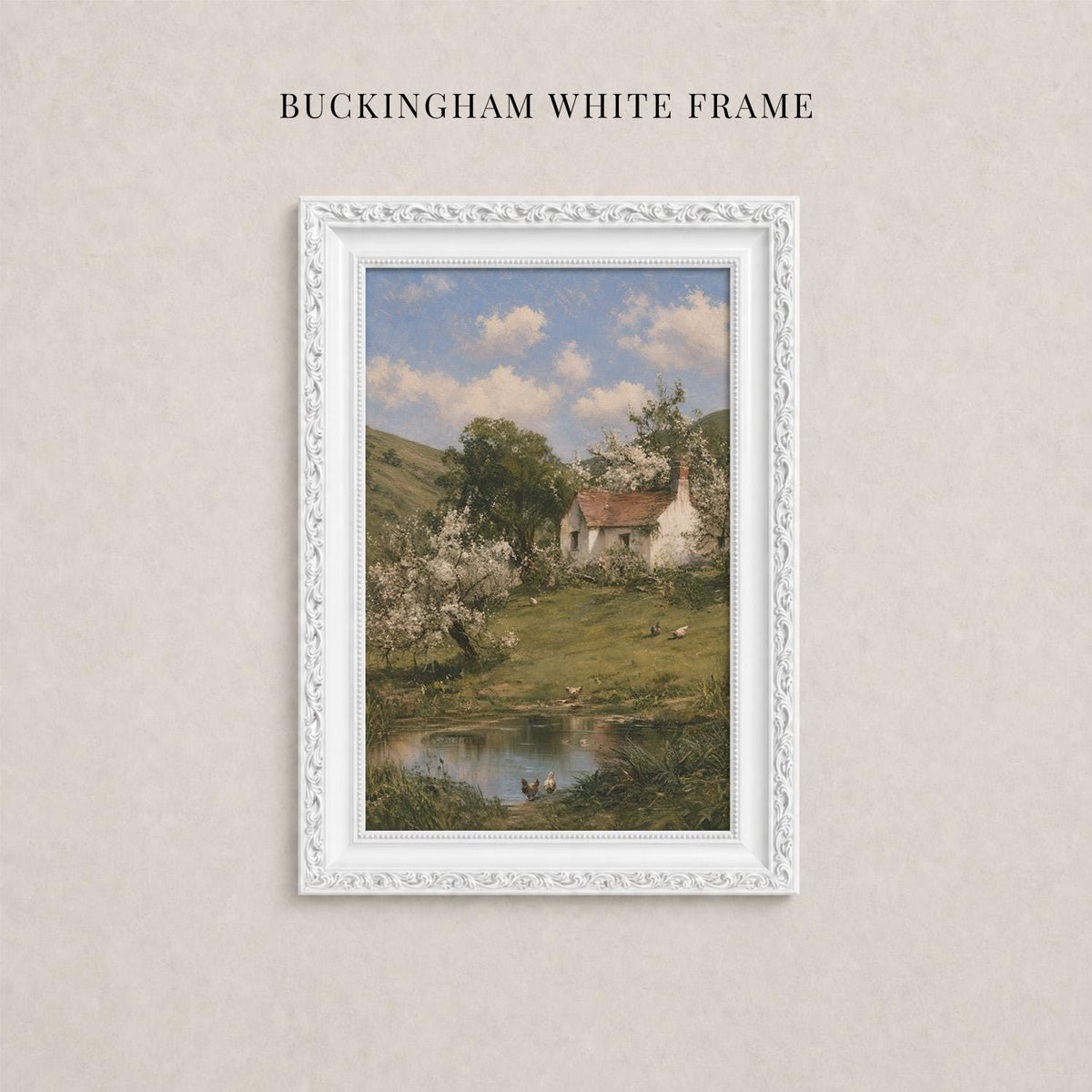 A white framed painting depicting a rural landscape with a pond, trees, and a small house in the background.