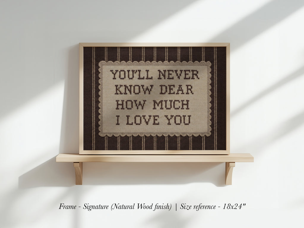 a framed sign with the text "YOU'LL NEVER KNOW DEAR HOW MUCH I LOVE YOU" displayed on a wooden shelf against a white wall.