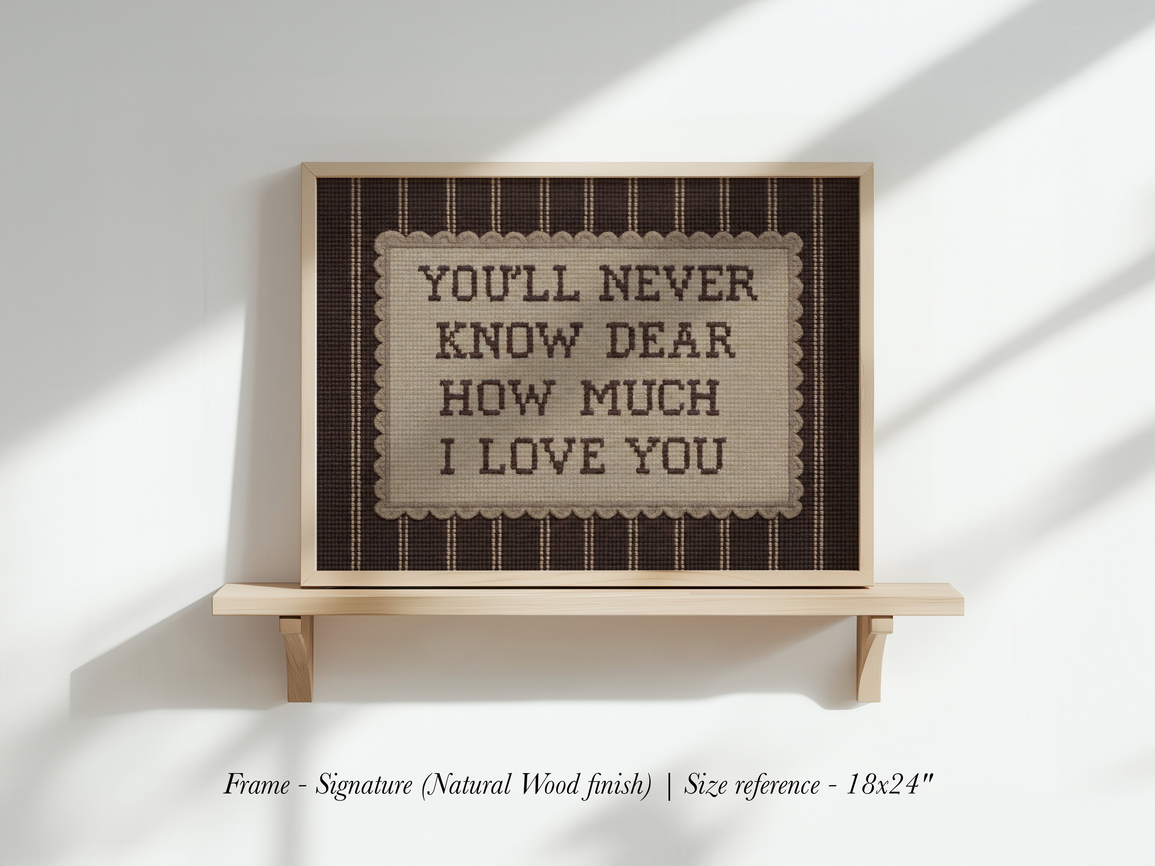 a framed sign with the text "YOU'LL NEVER KNOW DEAR HOW MUCH I LOVE YOU" displayed on a wooden shelf against a white wall.