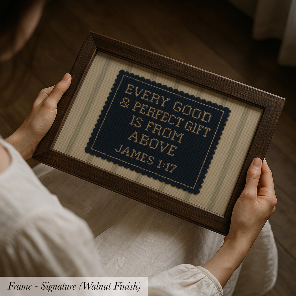 A person is holding a framed cross-stitch embroidery with the text "EVERY GOOD & PERFECT GIFT IS FROM ABOVE JAMES 1:17" on it.