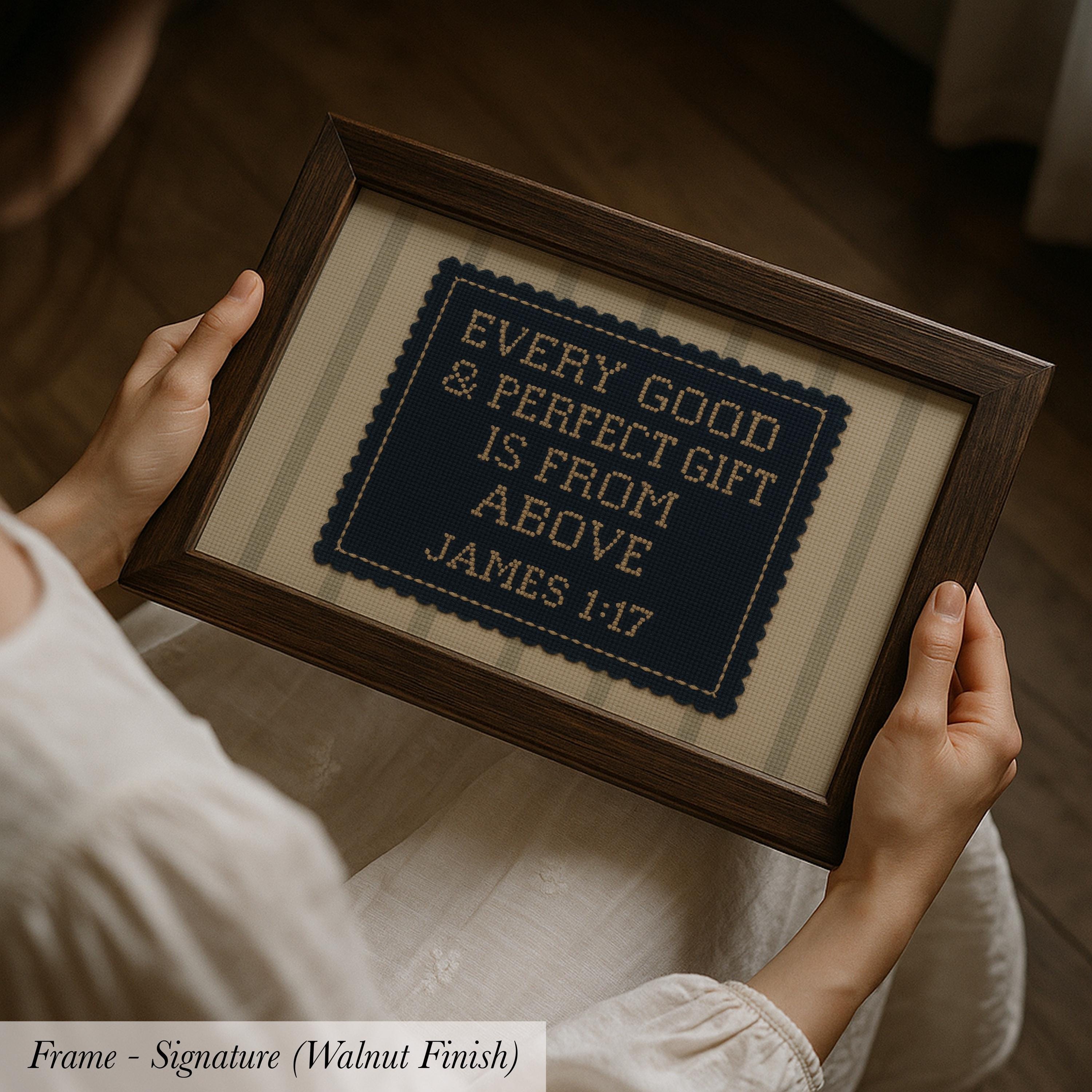 A person is holding a framed cross-stitch embroidery with the text "EVERY GOOD & PERFECT GIFT IS FROM ABOVE JAMES 1:17" on it.
