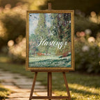 a wooden easel displaying a framed poster with text, standing on a stone path surrounded by flowers and greenery.