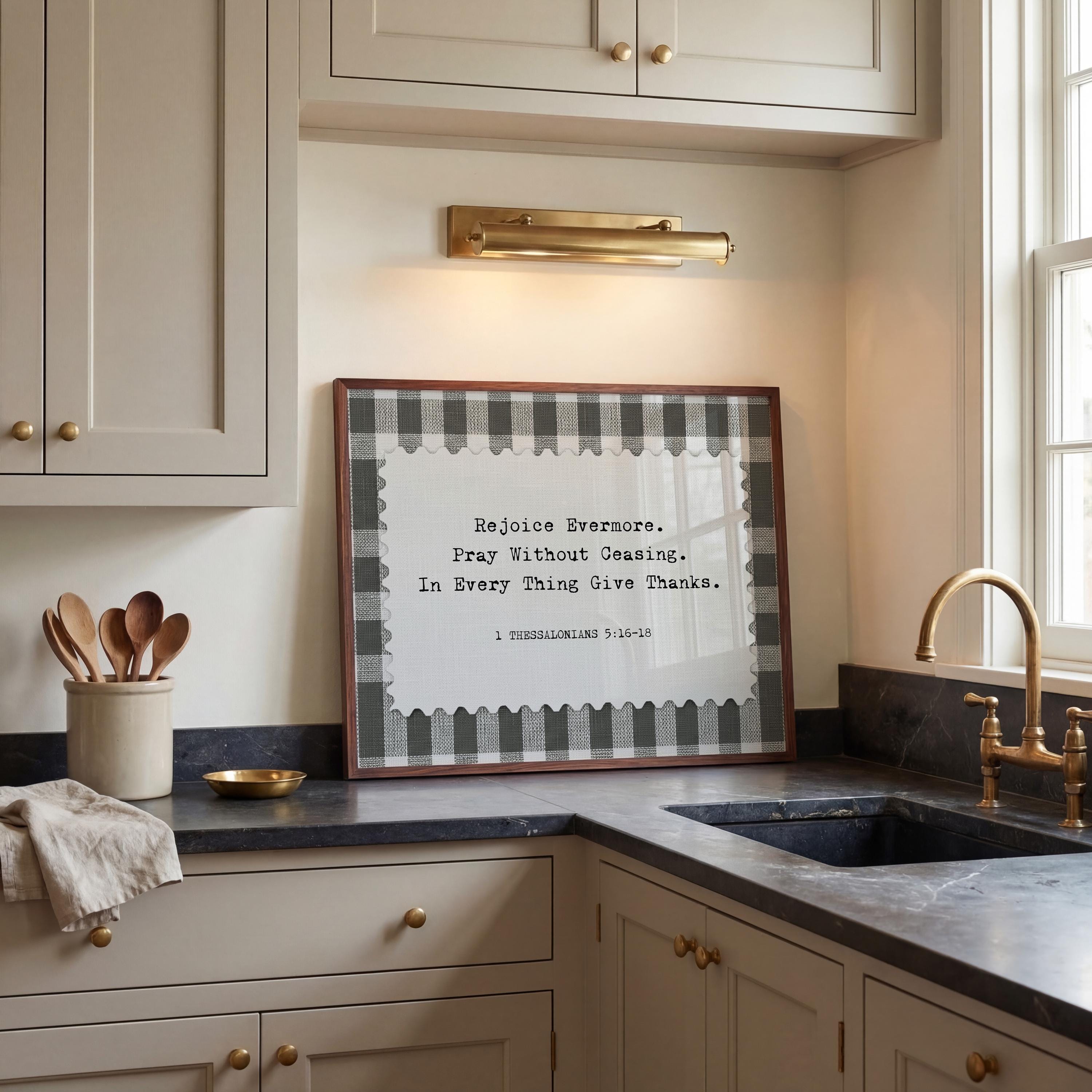 a kitchen counter with a framed quote that reads "Rejoice Everyday, Pray Without Coasting, In Every Thing Give Thanks." The quote is in black and white and is framed in a checkered pattern. The kitchen counter has a sink and various kitchen utensils, such as spoons, arranged on it.