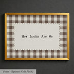A framed piece of paper with the text "How Lucky Are We" written on it, placed inside a gold-framed picture.