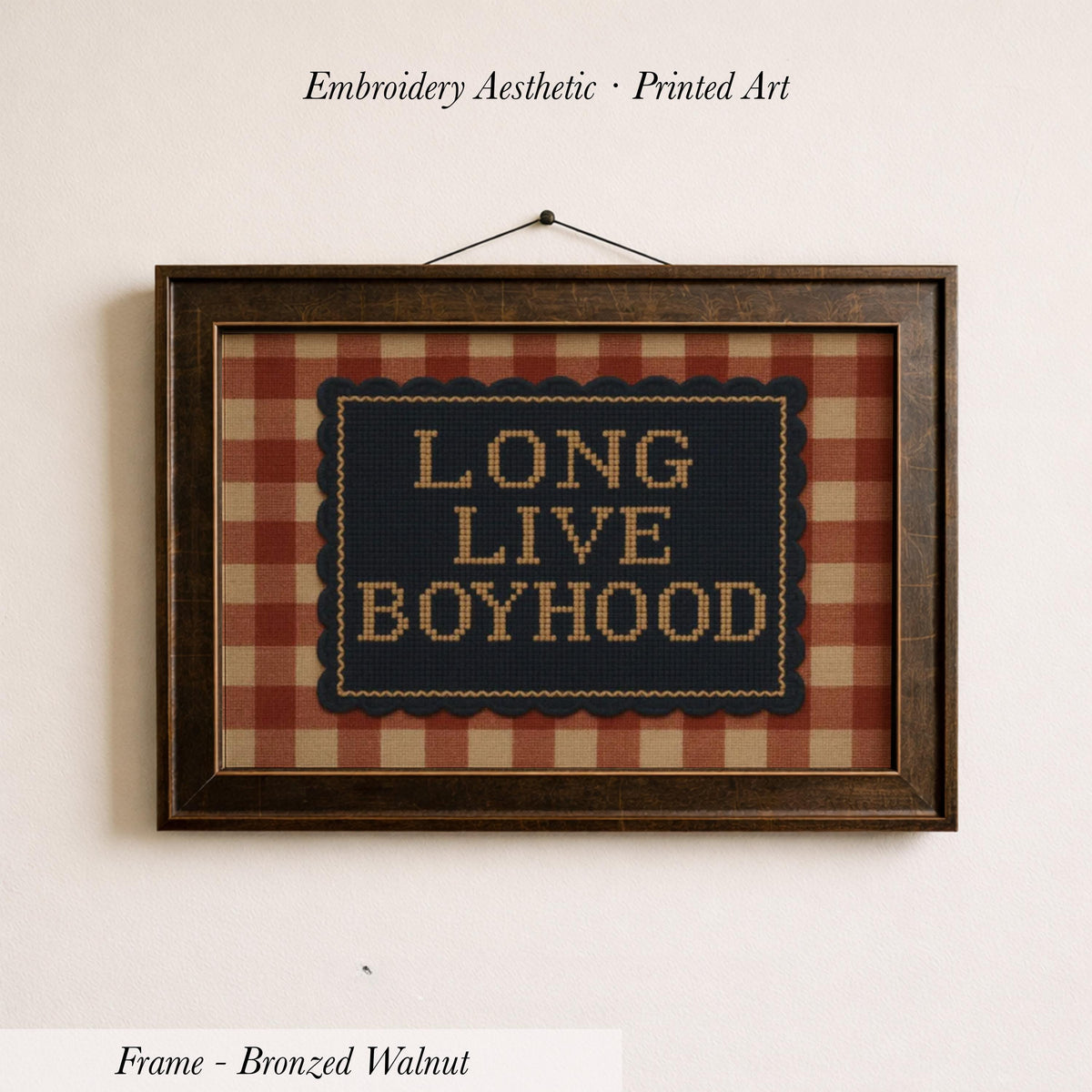 a framed embroidered design with the text "LONG LIVE BOYHOOD" on a plaid background.