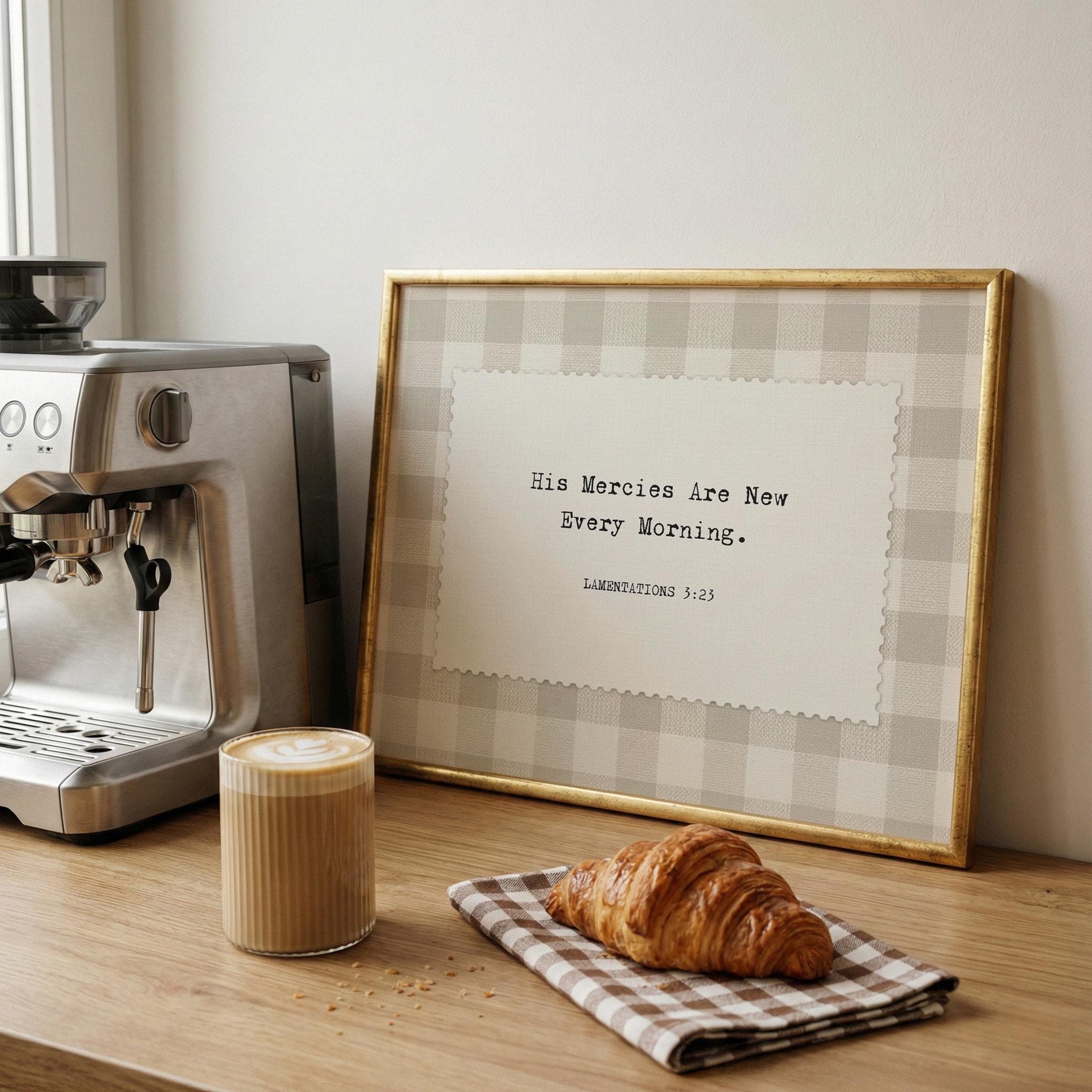 a wooden table with a croissant, a cup of coffee, and a framed quote, all set against a white wall.