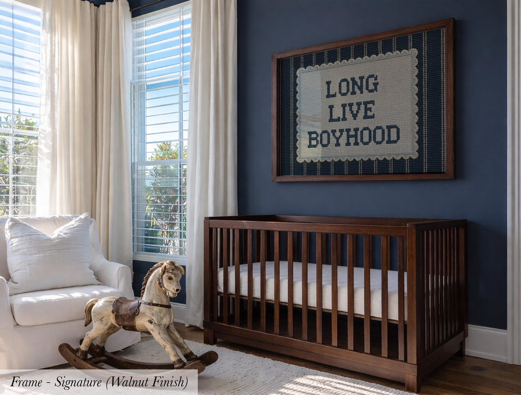 a nursery room with a wooden crib, a rocking chair, and a framed sign on the wall that reads "LONG LIVE BOYHOOD".