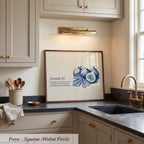 A framed print of a blue and white illustration of figs is displayed on a kitchen counter, accompanied by a quote about faith and trust.