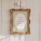 a gold-framed picture with a white border hanging on a white wooden wall. The picture contains a message that reads "YOU'LL NEVER KNOW DEAR HOW MUCH I LOVE YOU".