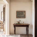 a wooden table with a bowl and a candle on it, set against a white wall with a framed picture hanging above it.