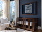 A wooden crib with a white mattress, a rocking horse, and a framed sign with the text "Little boy big dreams" on a blue wall.