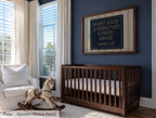 a nursery room with a wooden crib, a rocking horse, and a framed sign on the wall.