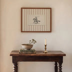 a cozy corner of a room with a wooden table, a framed picture, a candle, and a bowl of flowers.