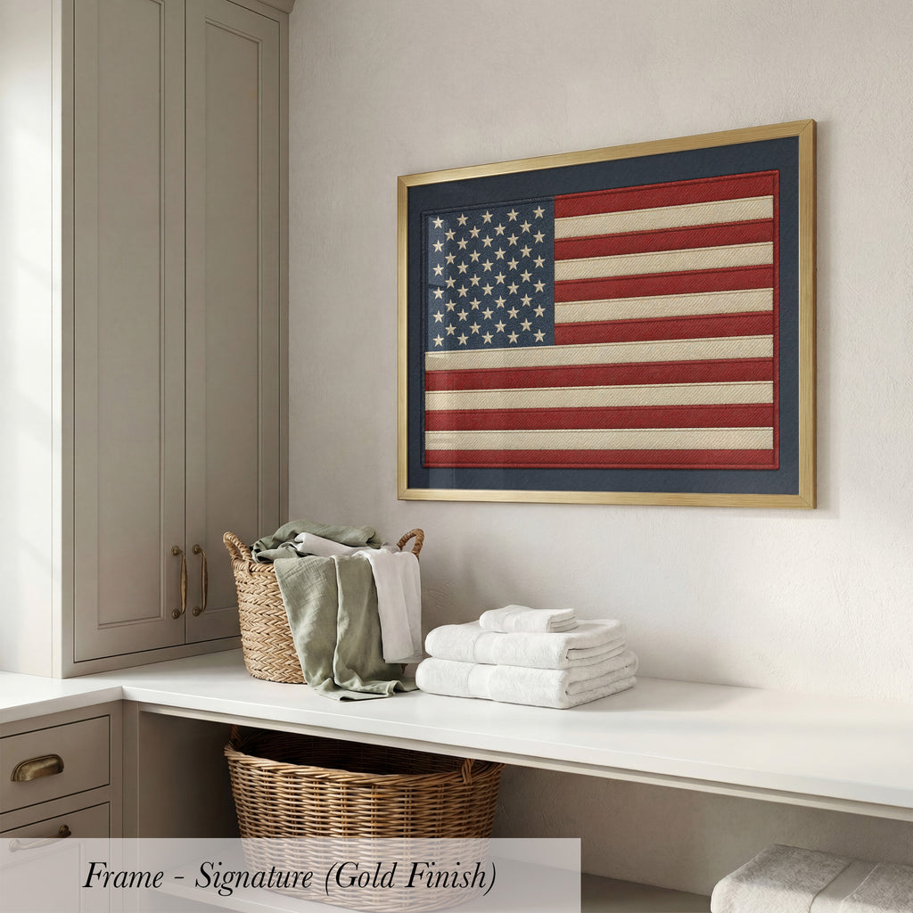 a framed American flag hanging on a wall above a white countertop with folded towels and a wicker basket.
