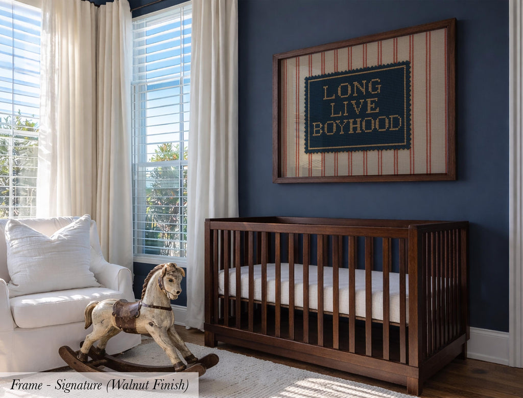 a nursery room with a wooden crib, a rocking chair, and a framed sign on the wall that reads "Long Live Boyhood".