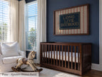 a nursery room with a wooden crib, a rocking chair, and a framed sign on the wall that reads "Long Live Boyhood".