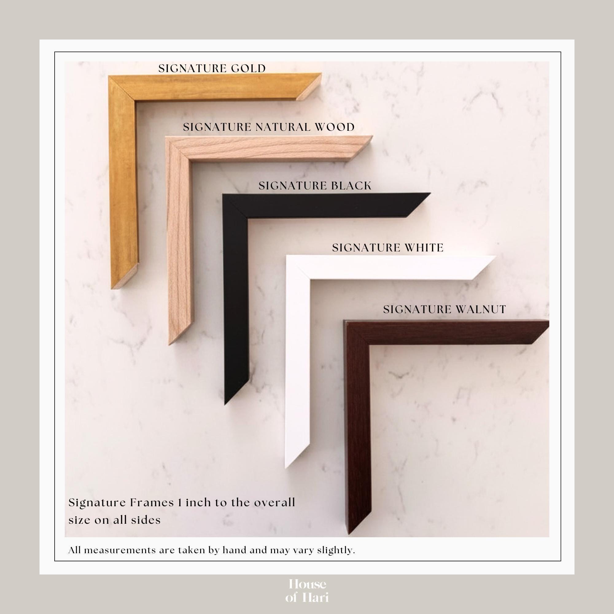 a collection of five signature frames in various colors and materials, including gold, natural wood, black, white, and walnut. The frames are arranged in a row, with the gold frame being the largest and the walnut frame being the smallest. The image also includes a caption that states all measurements are taken by hand and may vary slightly.