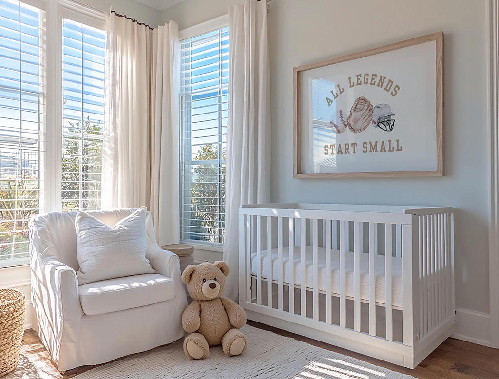 A cozy nursery with a white crib, a white chair, and a teddy bear. The room has large windows that let in natural light, and a framed quote on the wall that says "All legends start small".