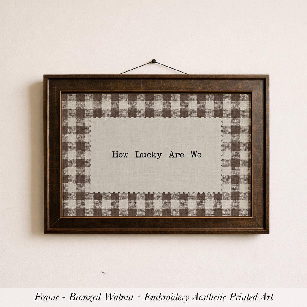 A framed piece of embroidered artwork with the text "How Lucky Are We" displayed on it.