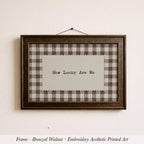 A framed piece of embroidered artwork with the text "How Lucky Are We" displayed on it.