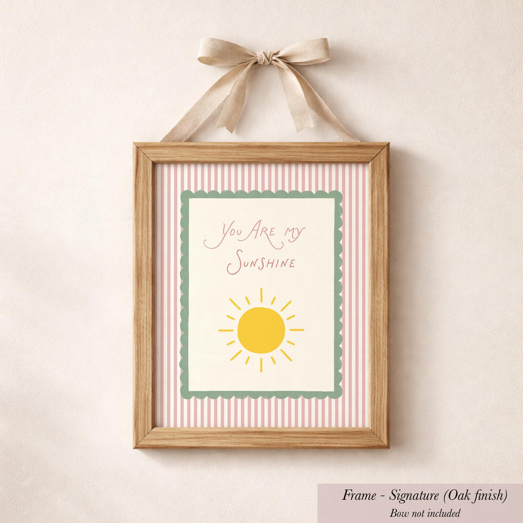 A framed picture with a pink and white striped border, featuring a yellow sun and the text "You are my sunshine" written in cursive.