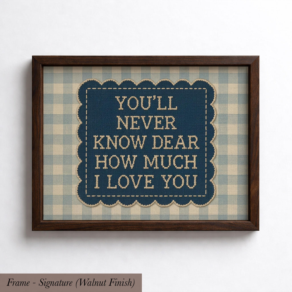 a framed piece of art with a blue background and a scalloped edge. The text within the frame reads "YOU'LL NEVER KNOW DEAR HOW MUCH I LOVE YOU".