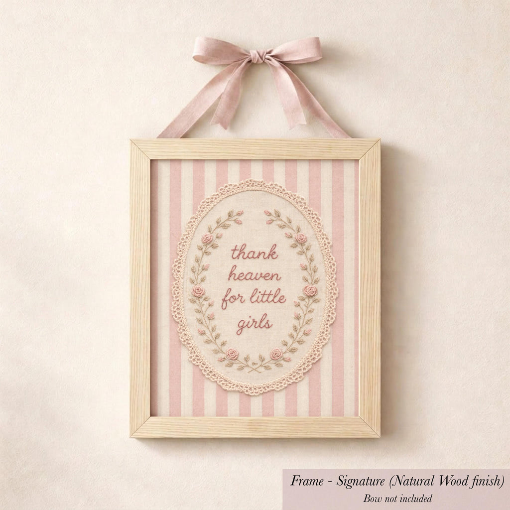 A framed picture with a pink ribbon and lace border, featuring a decorative floral design and the text "Thank heaven for little girls".
