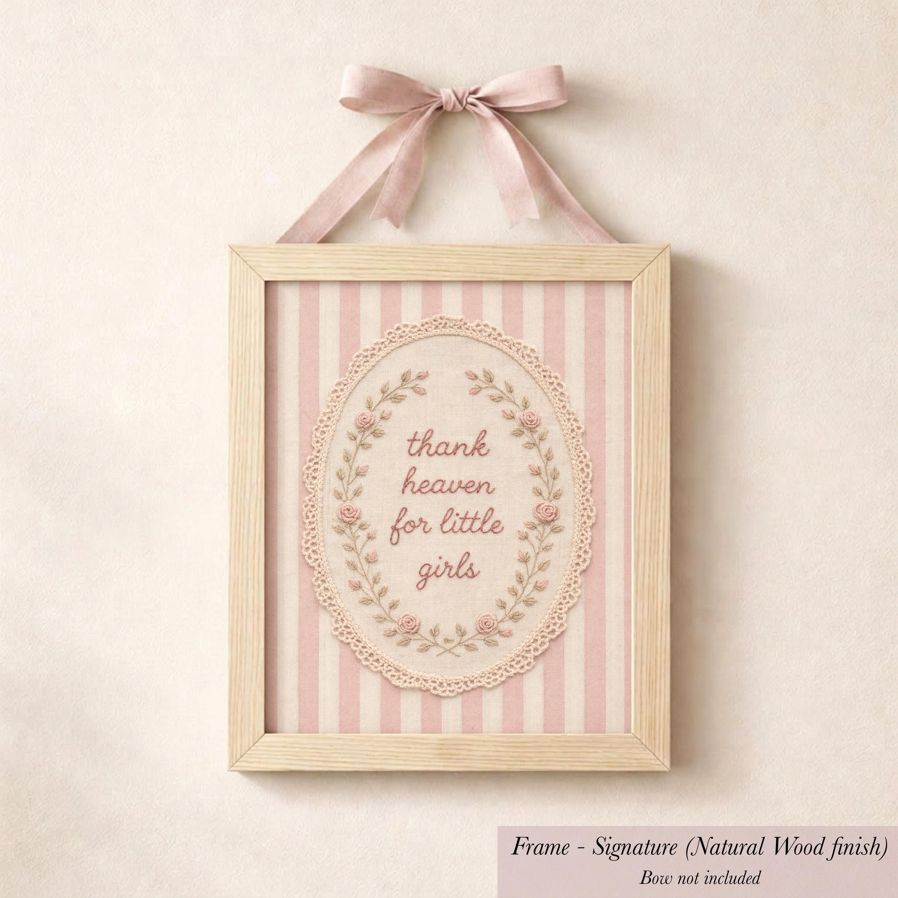 A framed picture with a pink ribbon and lace border, featuring a decorative floral design and the text "Thank heaven for little girls".