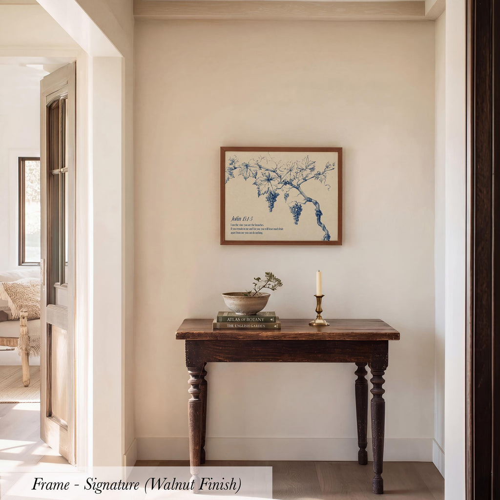 a wooden table with a bowl and a candle on it, set against a white wall with a framed artwork hanging above it.
