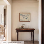 a wooden table with a bowl and a candle on it, set against a white wall with a framed artwork hanging above it.