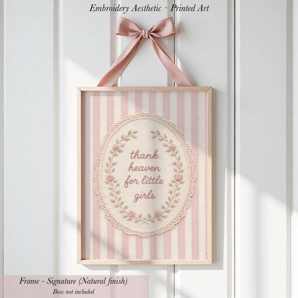 a framed embroidered art piece with a pink and white striped background and a lace border. The text on the art piece reads "Thank heaven for little girls".
