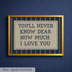 a framed cross-stitch design with the text "YOU'LL NEVER KNOW DEAR HOW MUCH I LOVE YOU" written on it.