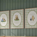 three framed canvas prints of Winnie the Pooh illustrations, hanging on a wall above a wooden crib.