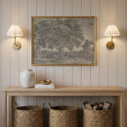 a wooden console table with a framed picture of a tree hanging above it, flanked by two wall sconces. The table also has a white vase, a stack of books, and three woven baskets.