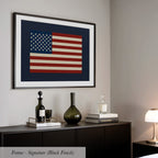 a framed artwork of the American flag hanging on a wall above a black dresser with various decorative items on top.
