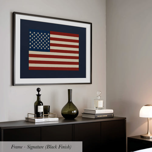 a framed artwork of the American flag hanging on a wall above a black dresser with various decorative items on top.