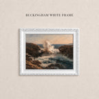 A white framed painting depicting a rocky coastline with crashing waves, hanging on a beige wall.