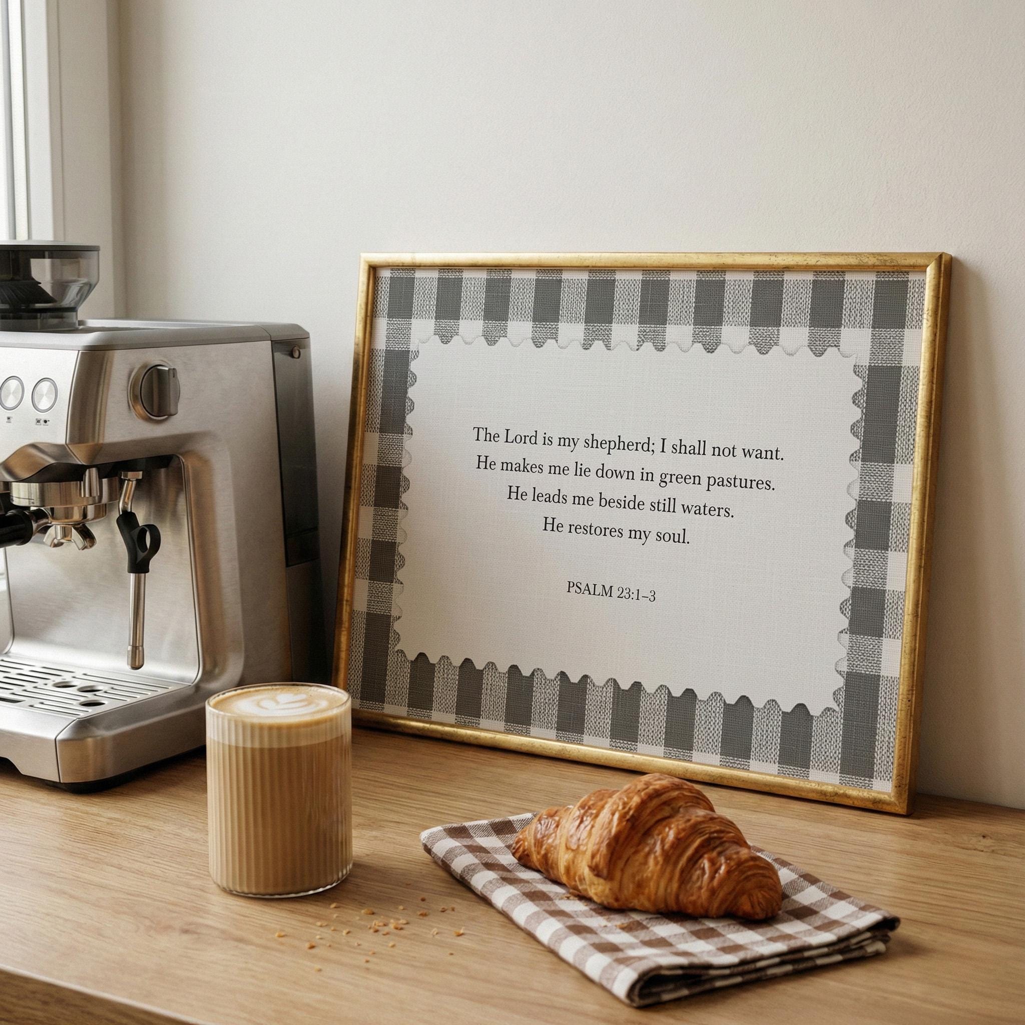 a framed Bible verse, a croissant, and a cup of coffee on a wooden table.