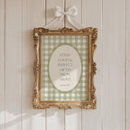 a gold-framed picture hanging on a white wooden wall. The picture has a green and white checkered pattern and contains a quote about gifts from above.