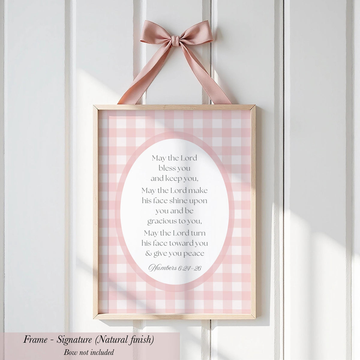 A framed sign with a pink and white checkered background hangs on a white wall. The sign contains a religious message, and the frame is described as a "Signature (Natural finish)" without further details.