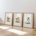 Three framed pictures of teddy bears in various poses, including one holding a baseball, are displayed on a wooden floor against a white wall.