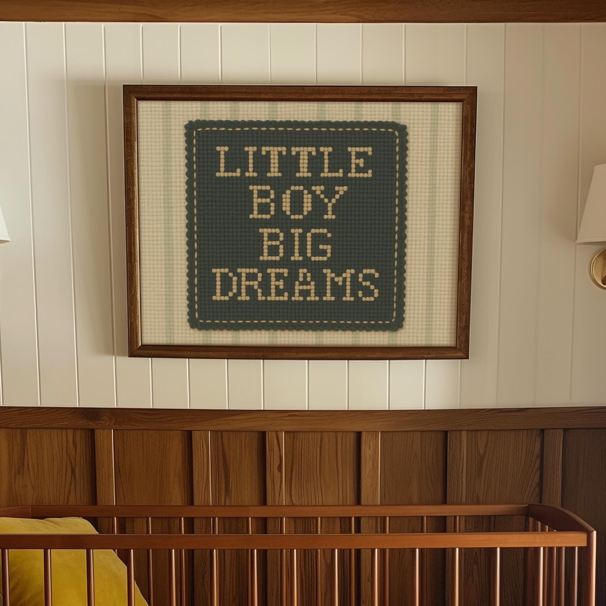 a framed cross-stitch design with the text "LITTLE BOY BIG DREAMS" on it, hanging on a wall above a wooden crib.