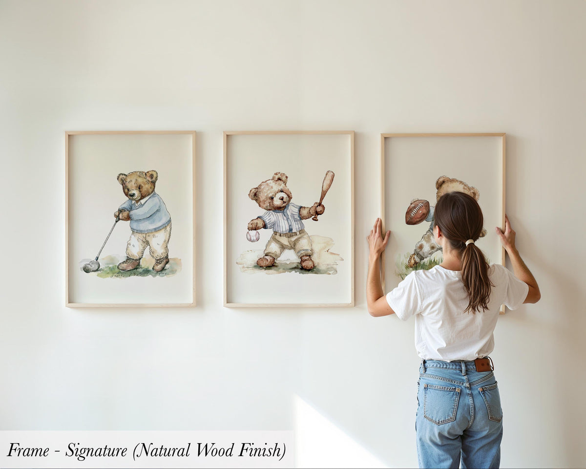 A woman is hanging three framed pictures on a wall, each depicting a teddy bear in different poses.